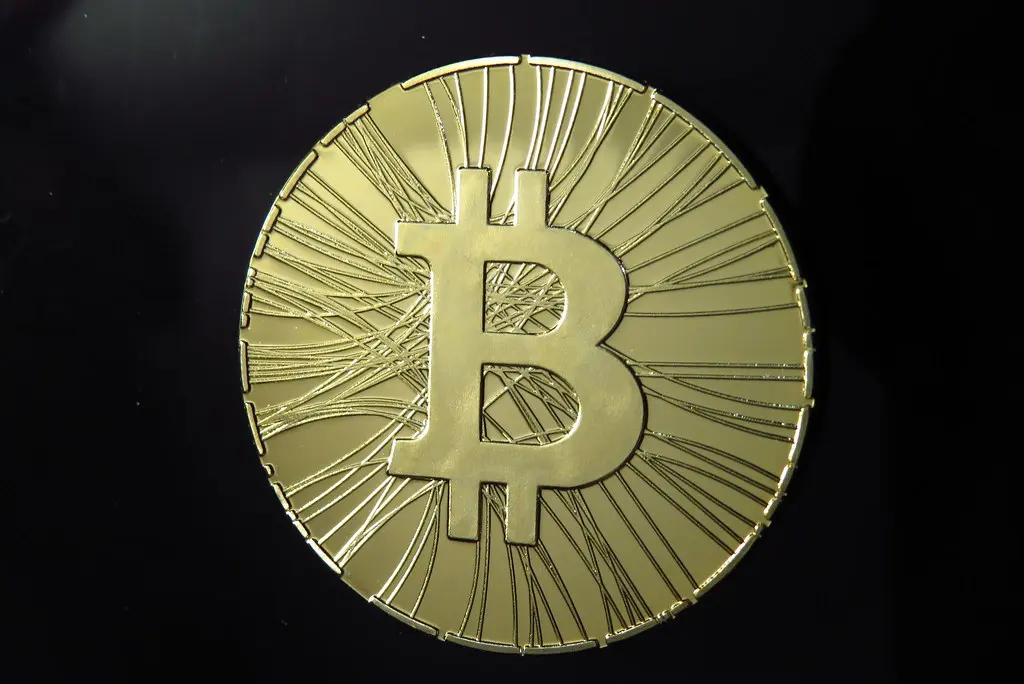 A gold-colored physical Bitcoin token with the symbol centered on a dark background.