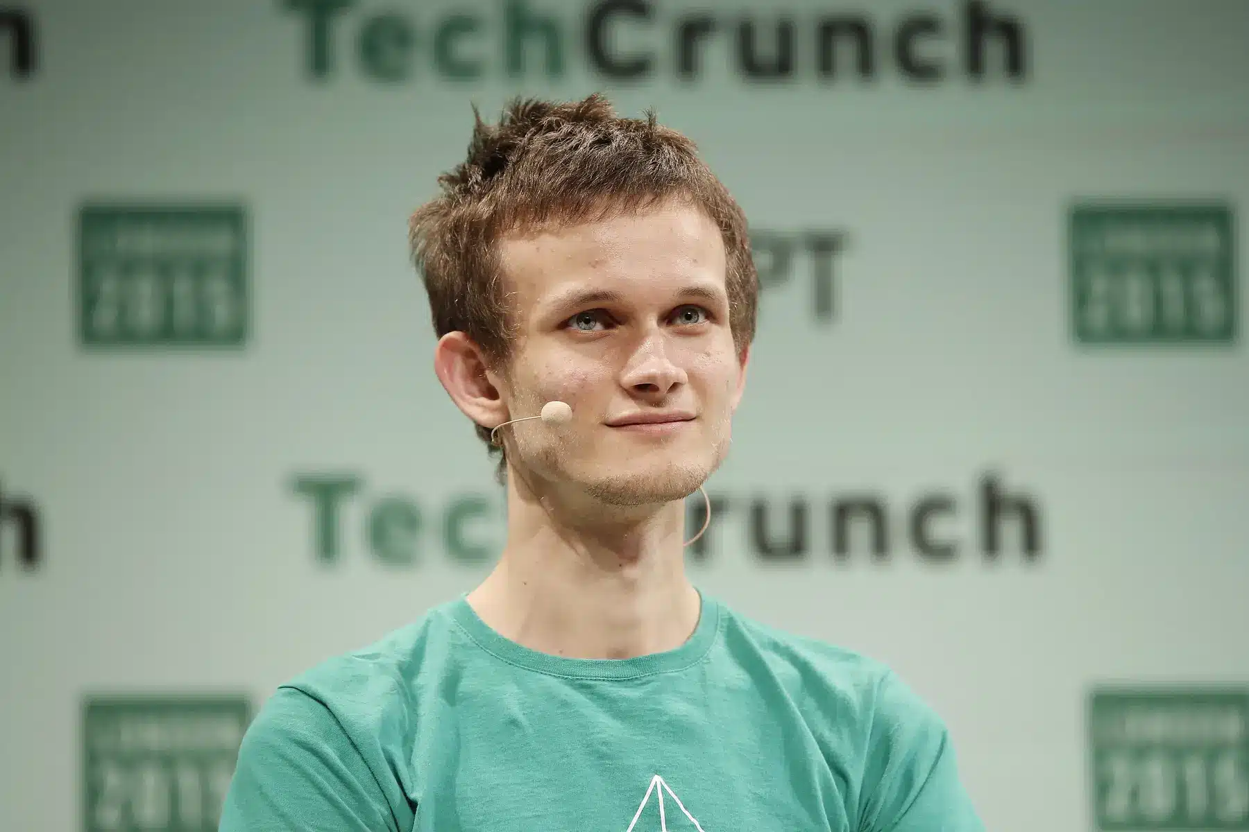 Vitalik Buterin wearing a green t-shirt and a headset microphone at TechCrunch London 2015.